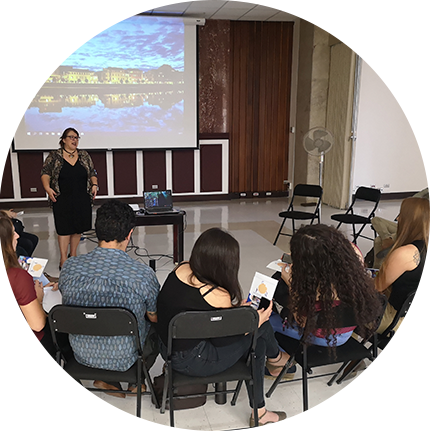 varias personas sentadas viendo a una señora que está al frente exponer.
