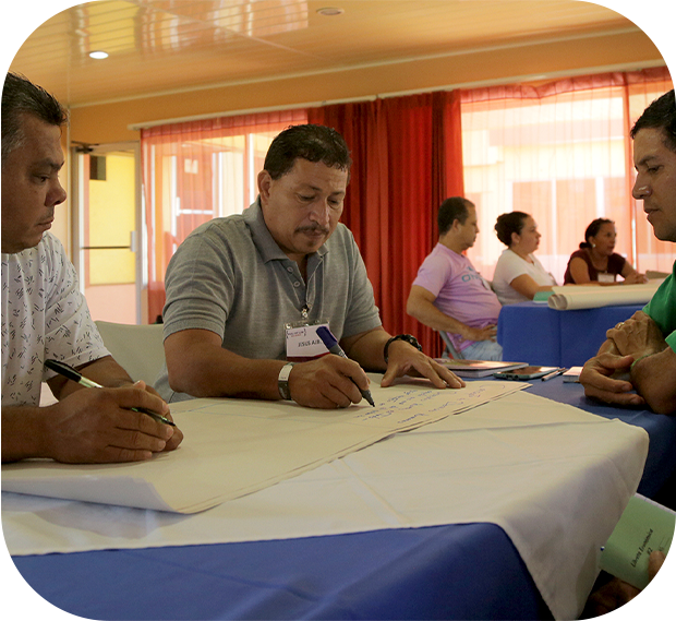 cuatro hombres escribiendo y conversando en una mesa, están trabajando juntos