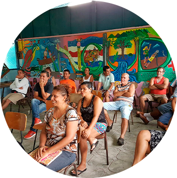 varias personas sentadas en un aula, hay una mujer sonriendo con un libro en su regazo.