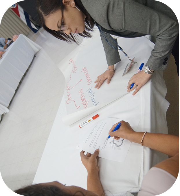 Personas reunidas alrededor de tres mesas, hablando, algunas sentadas y otras de pie.