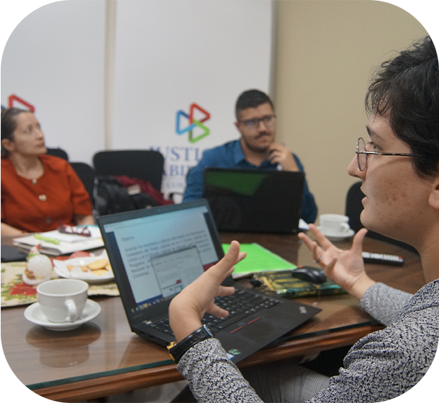 Hombre con su computadora personal, conversando con varias personas en la oficina.